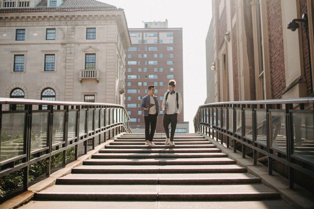Full length of students in casual clothes walking downstairs and talking in residential district in city in daytime